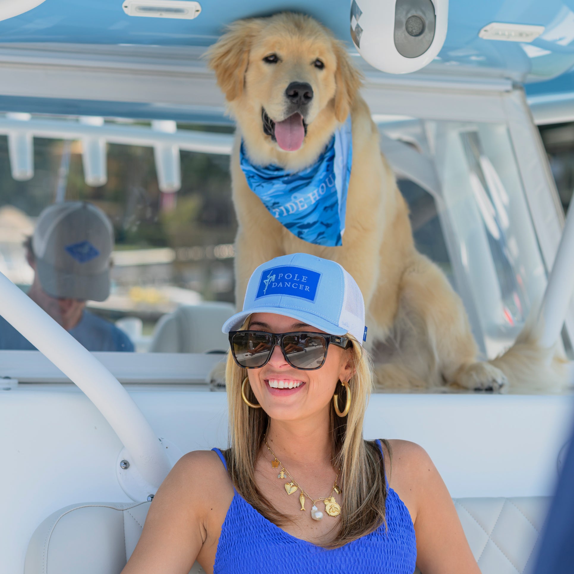 Woman with a dog on a boat wearing a wahoo Pole Dancer Alpha Trucker Hat with a blue patch.