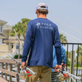 Man wearing the Navy/Heather Pole Dancer Alpha Long Sleeve Performance shirt while walking on a dock carrying several fishing poles.