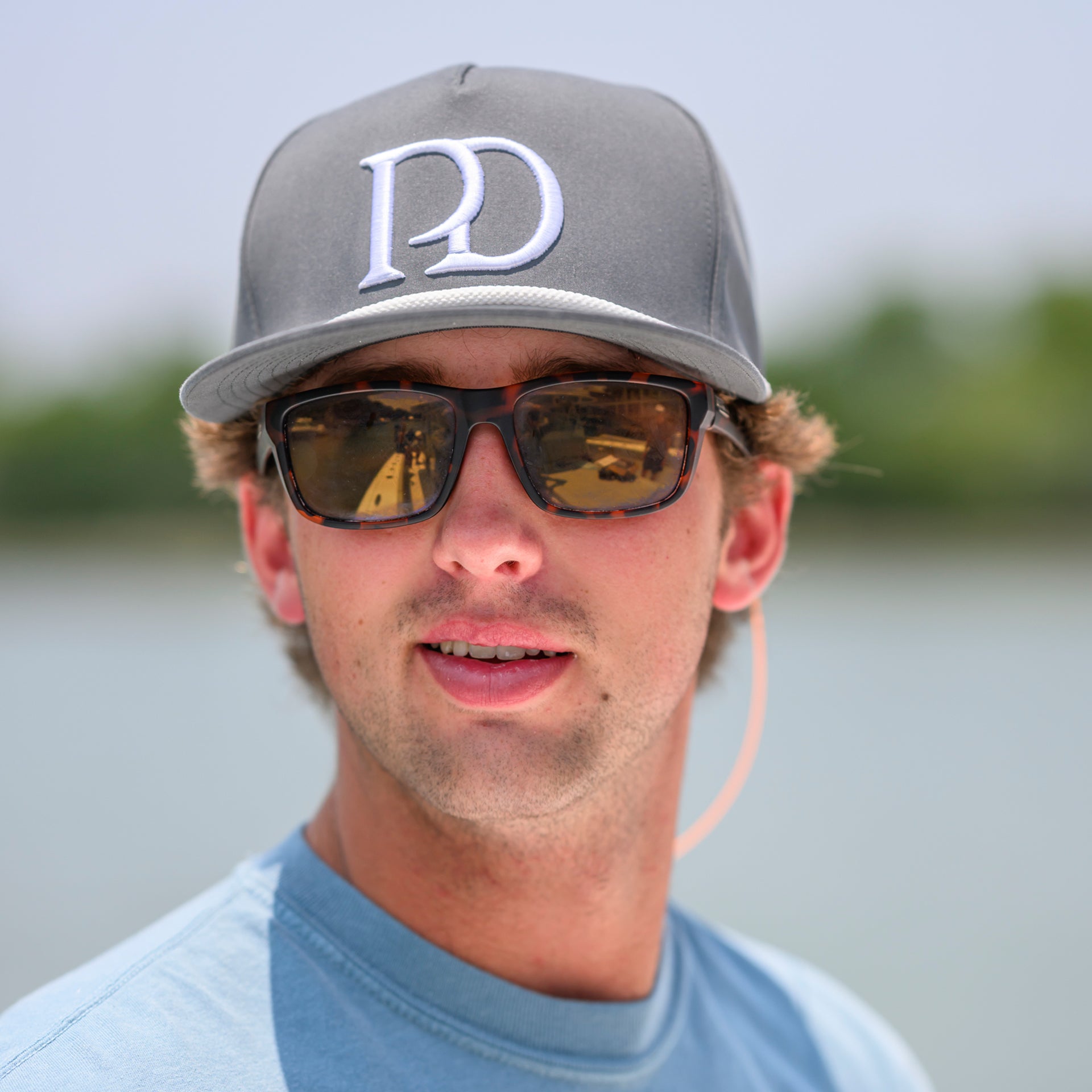 Man wearing the Pole Dancer Large PD Rope Hat and sunglasses on a boat with water in the background.